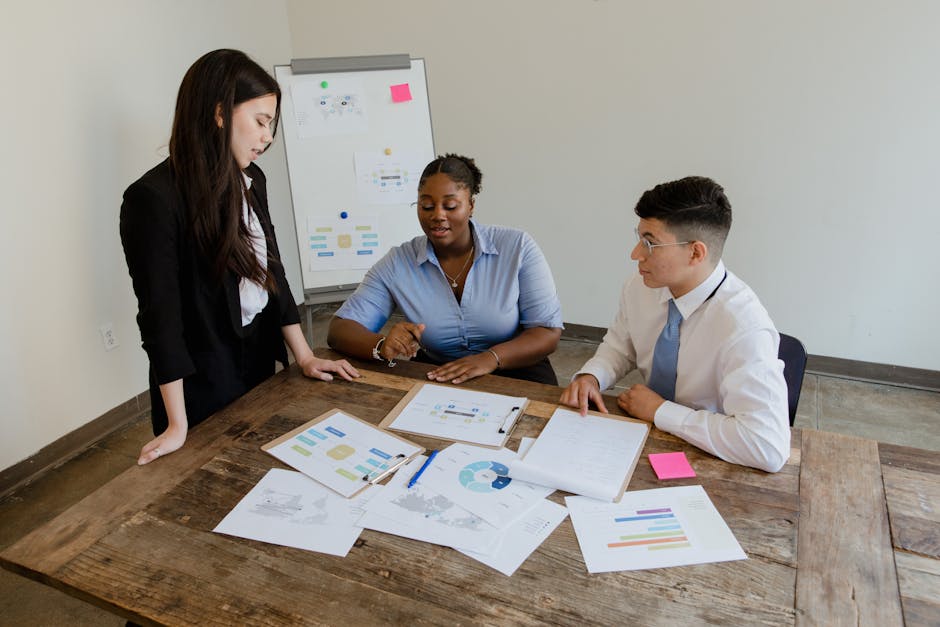 Three colleagues discussing work documents at a table, emphasizing teamwork and diversity.